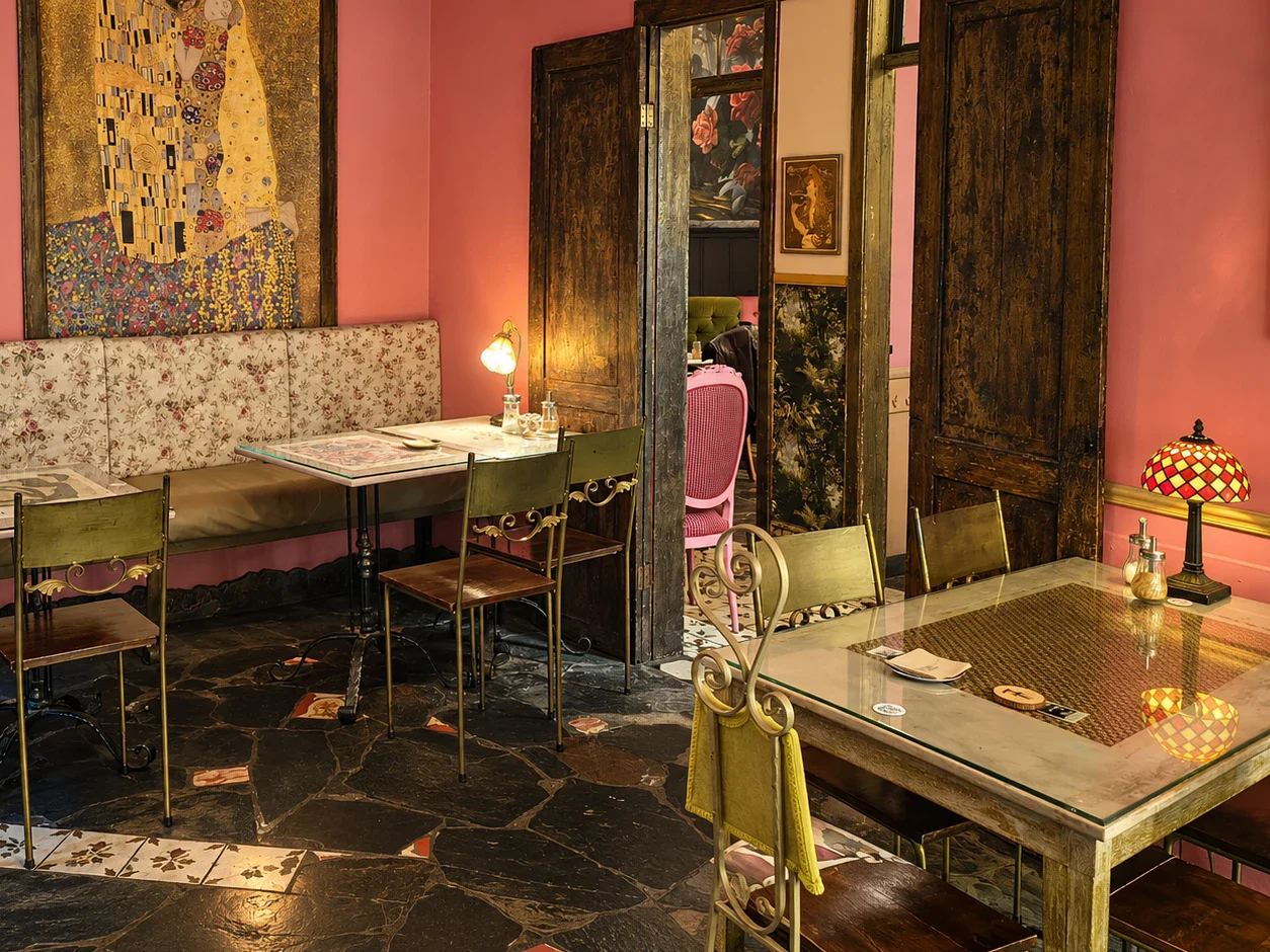 El salón rosa: banco tapizado de flores, mesas con sobre de cristal, sillas de hierro verde y lámparas encendidas